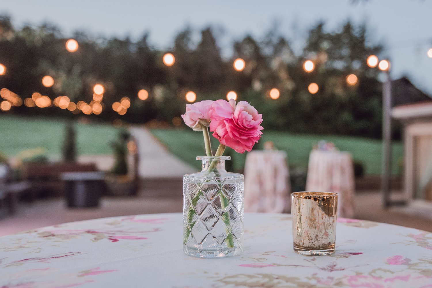 Two pink roses in a glass vase outside on a table